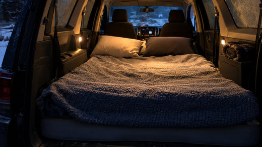 Foam mattress bed made up in the back of a minivan at a cold forest campsite at night
